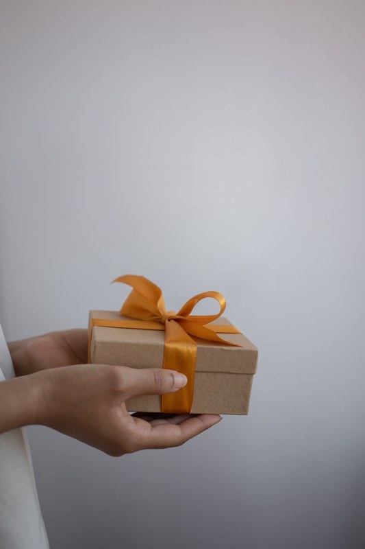 Hands holding out a small gift box tied with an orange ribbon